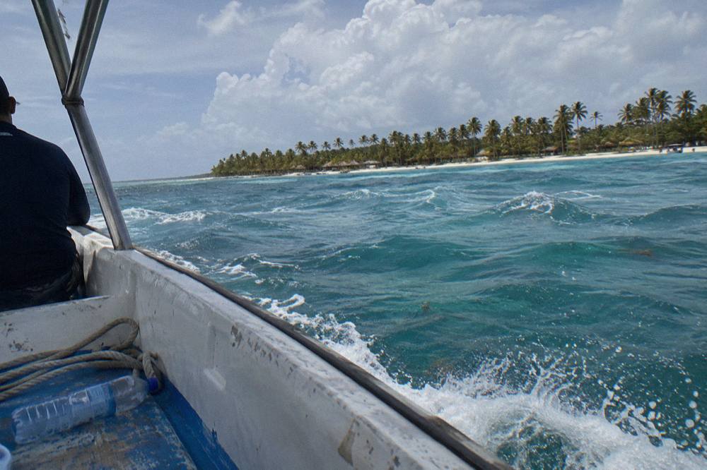 A speedboat crossing turquoise water toward a palm-fringed island beach