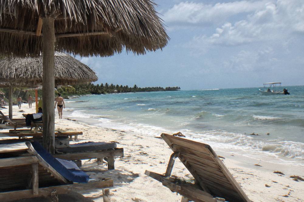 Wooden lounge chairs and thatched palm umbrellas along a wide white beach