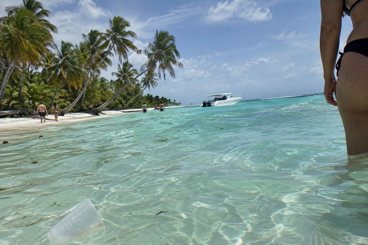 Turquoise shallow water at a sandbar with a white boat anchored in the distance