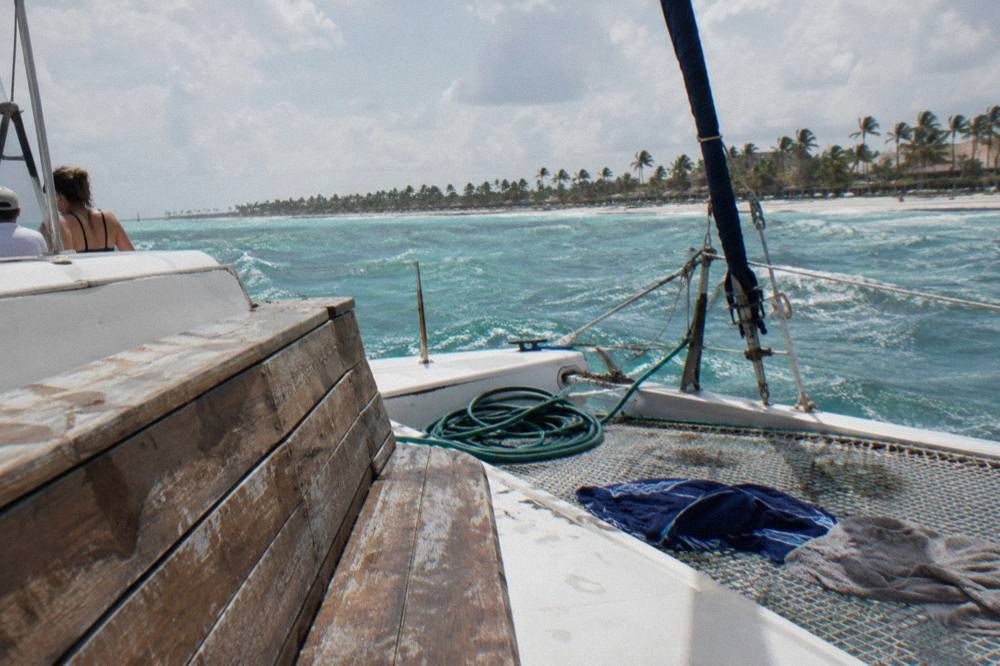 Catamaran deck with wooden bench seating and rigging seen from the bow in morning light