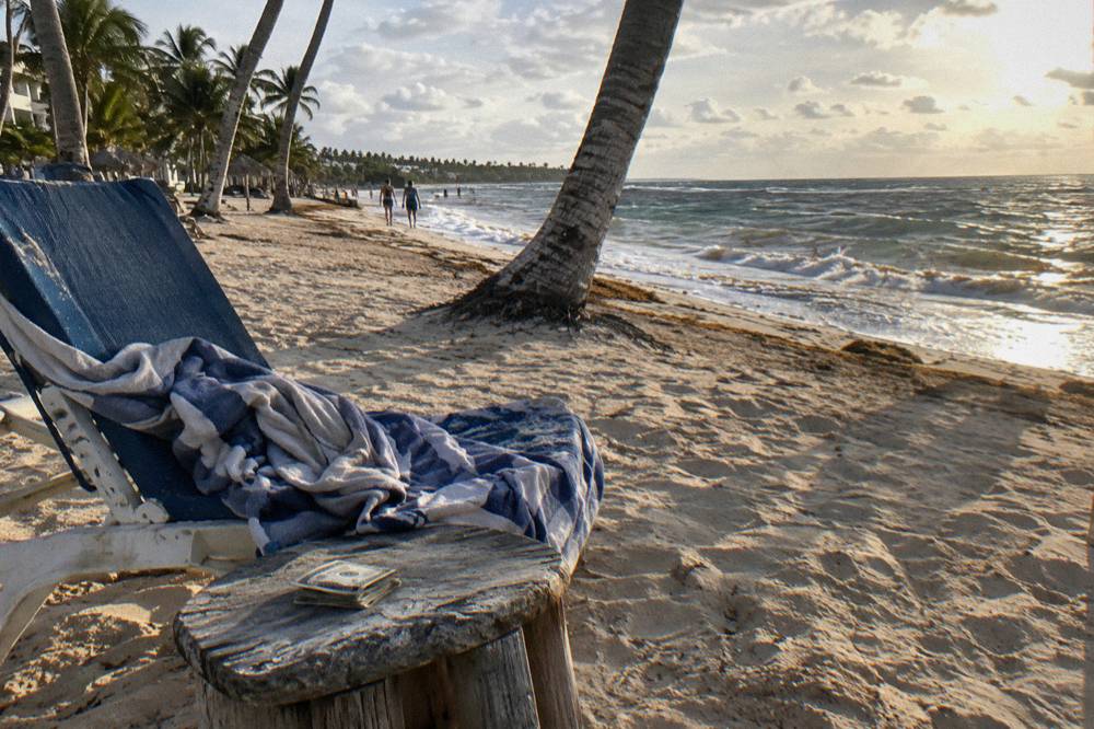 Beach chair with a towel and a folded stack of small bills on a wooden side table