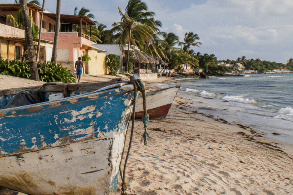 Wooden fishing boats resting on sand in front of colorful beachside buildings under palm trees