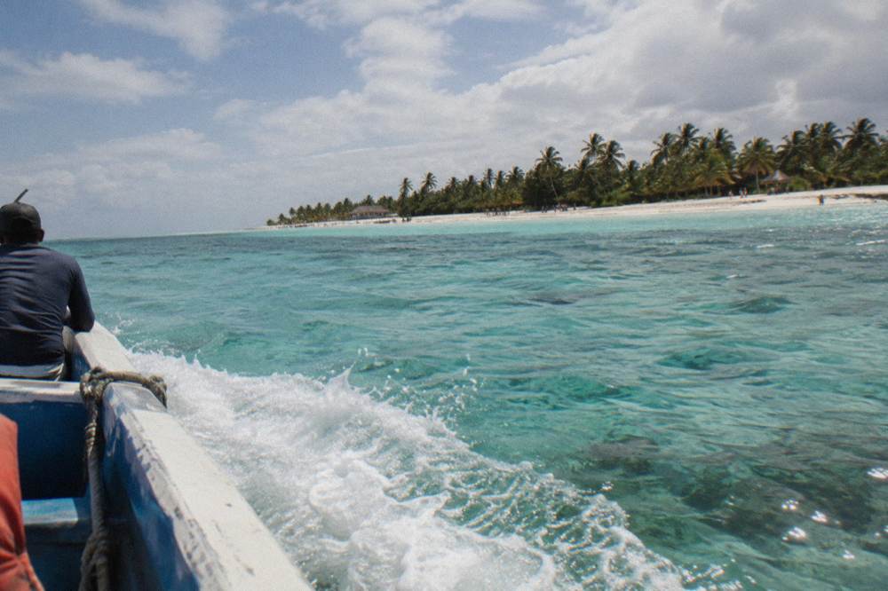 Speedboat crossing calm shallow turquoise water toward a palm-fringed sandbar