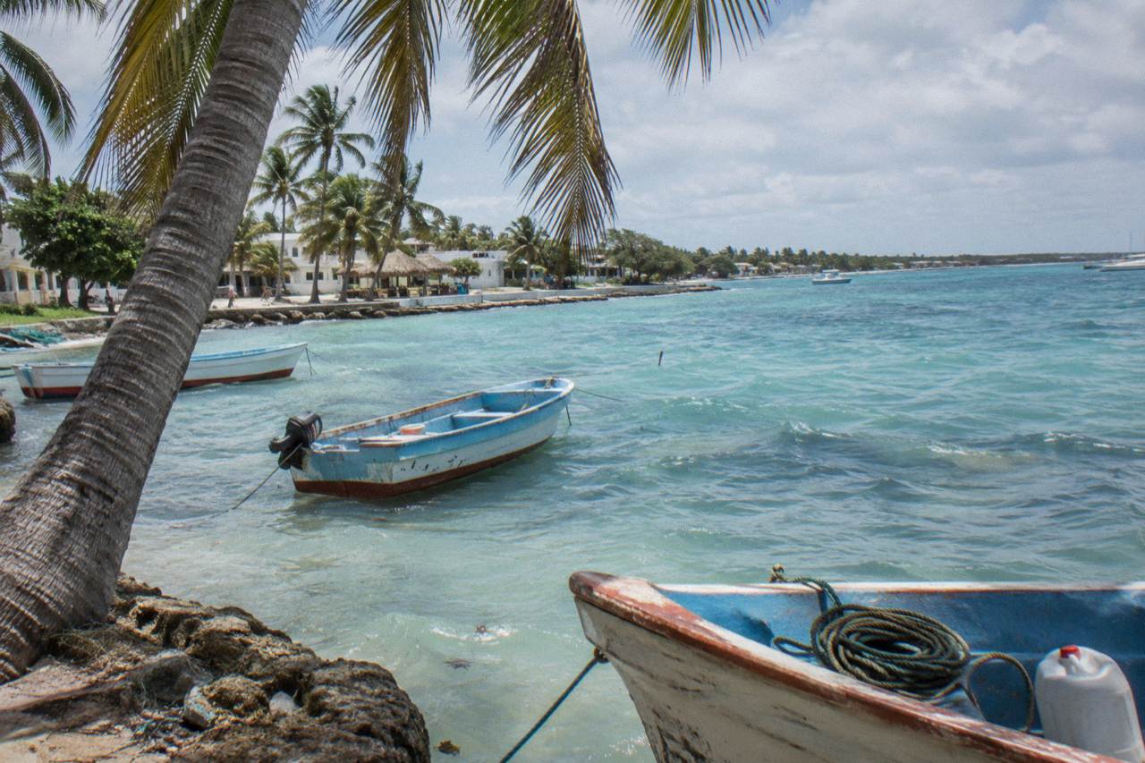 Small fishing boats moored in calm turquoise water beside a palm-lined beach at midday