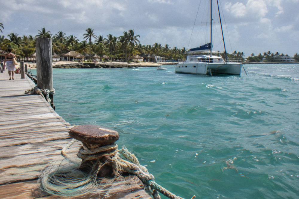 A wooden pier extending over turquoise water with a catamaran moored offshore