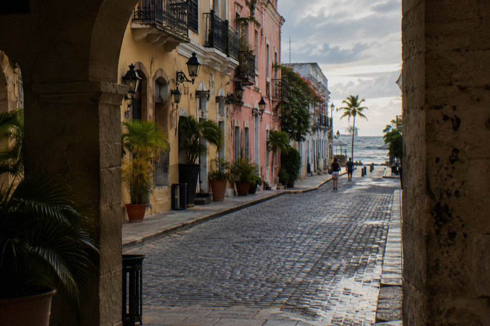 A stone colonial street with pastel facades and iron lampposts in evening light