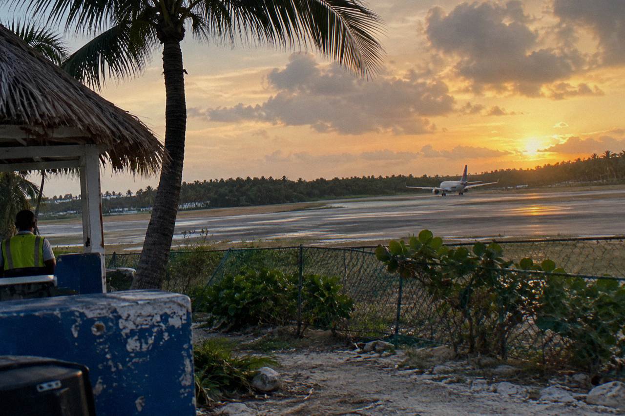 A tropical airport runway at golden hour with palm trees along the edge