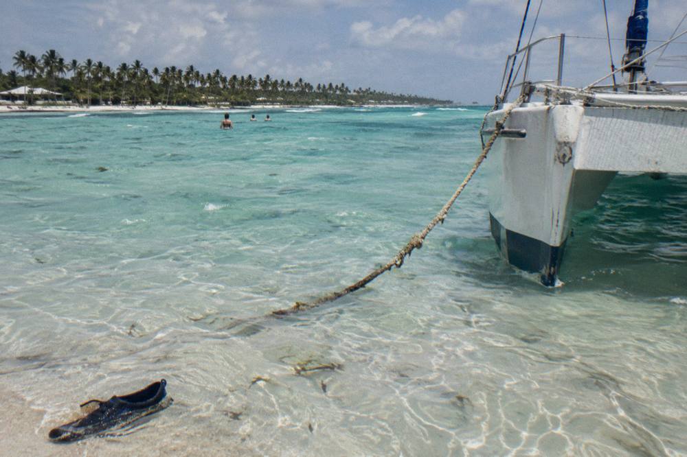 Catamaran anchored in shallow turquoise water near a sandbar with palm trees on the horizon
