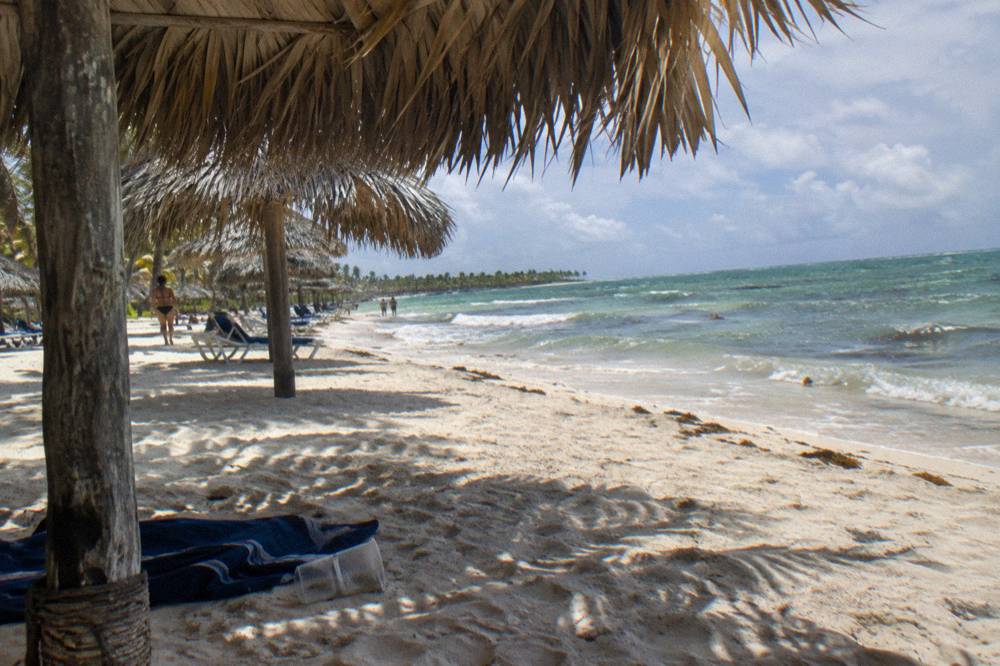 Shaded thatched palm umbrellas in a row along a white sand beach with calm green-blue water beyond