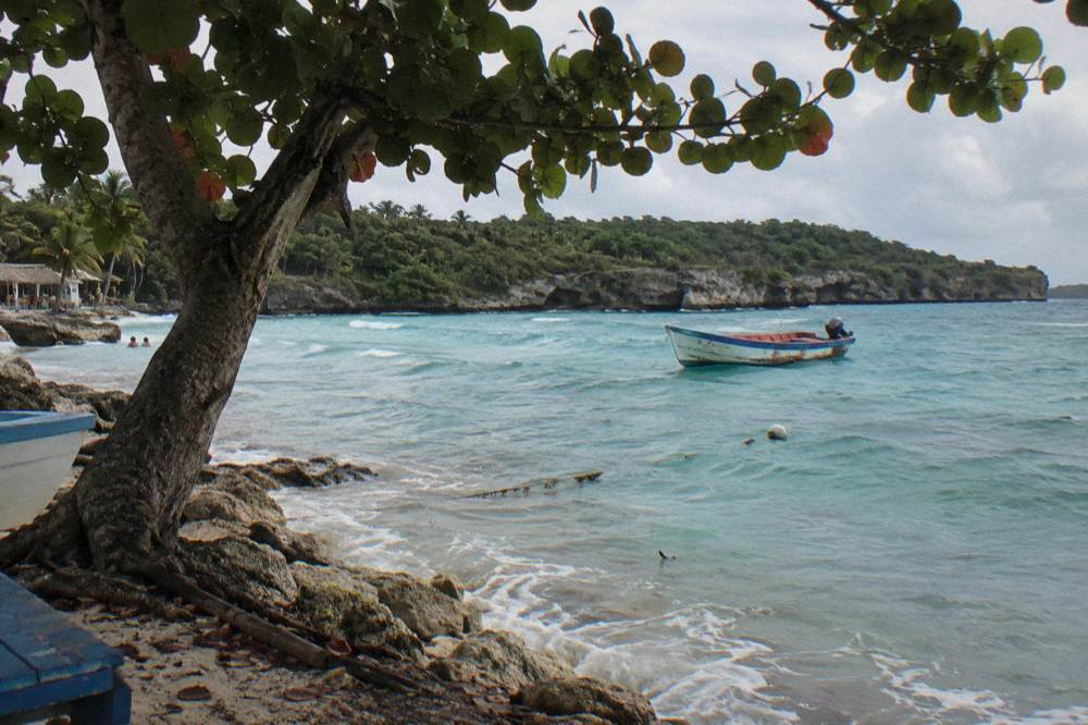 Turquoise bay with a small boat anchored offshore and forested hills behind.