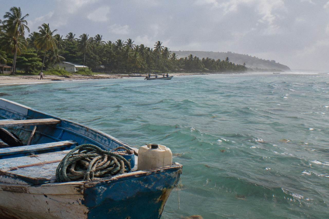 Wooden boat resting in calm turquoise water beside a palm covered peninsula shoreline.