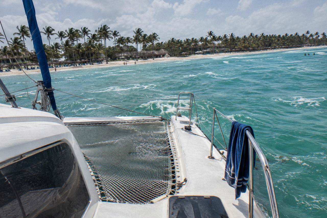A large sailing catamaran anchored in calm turquoise water near a palm-lined beach