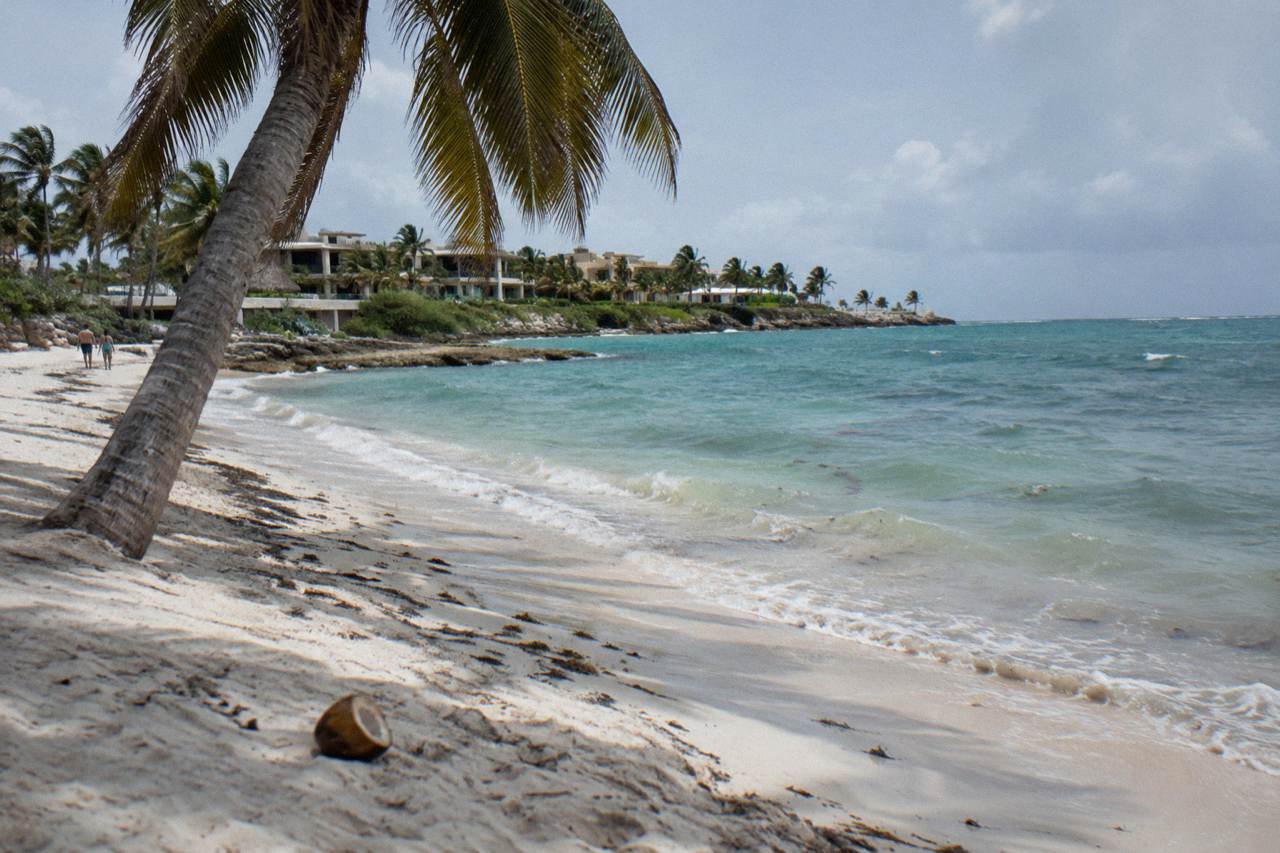 Wide Caribbean beach with pale sand, leaning palms and calm turquoise water along an empty shoreline