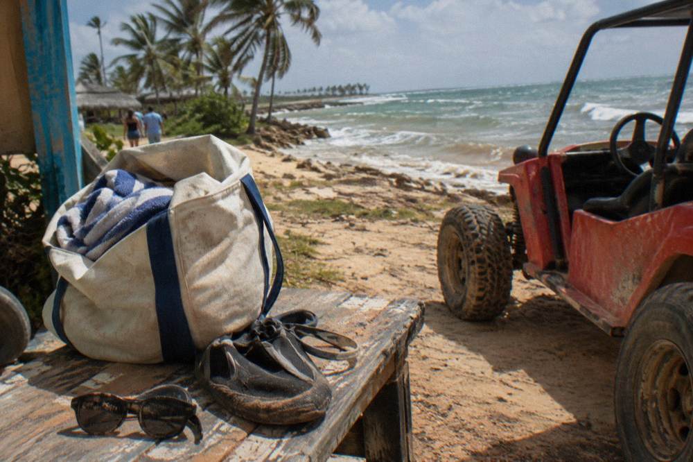 Beach bag with towel, water shoes and sunglasses on a wooden bench beside a parked buggy