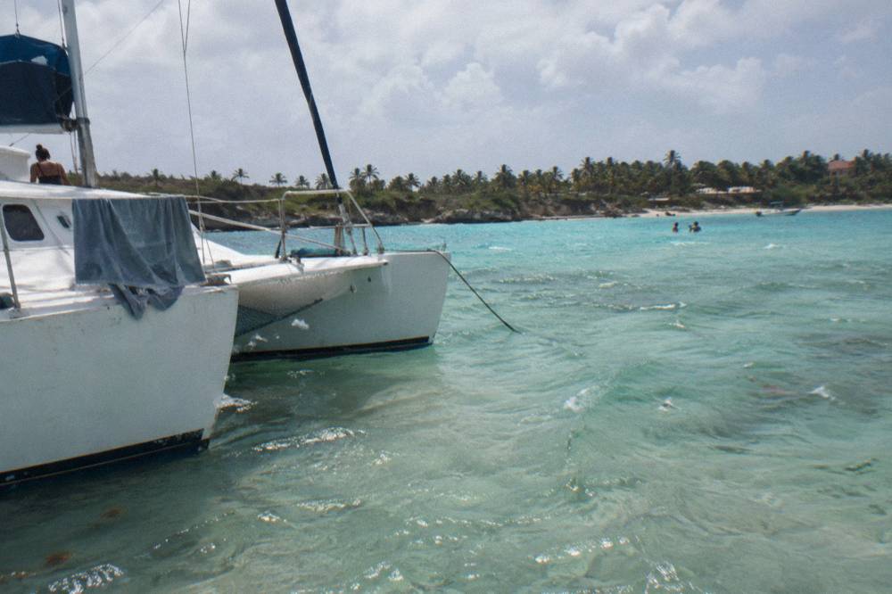 Catamaran anchored near a sandbar in shallow turquoise water with distant palm-covered island