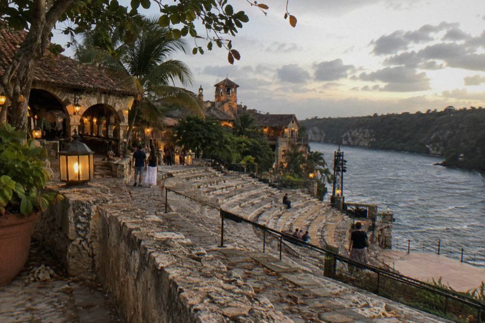 Evening view of a riverside stone village with warm lights and an open-air amphitheater