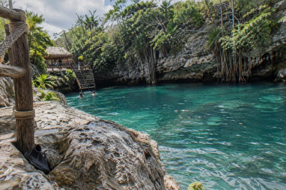 A turquoise freshwater cenote surrounded by limestone cliffs and tropical vegetation