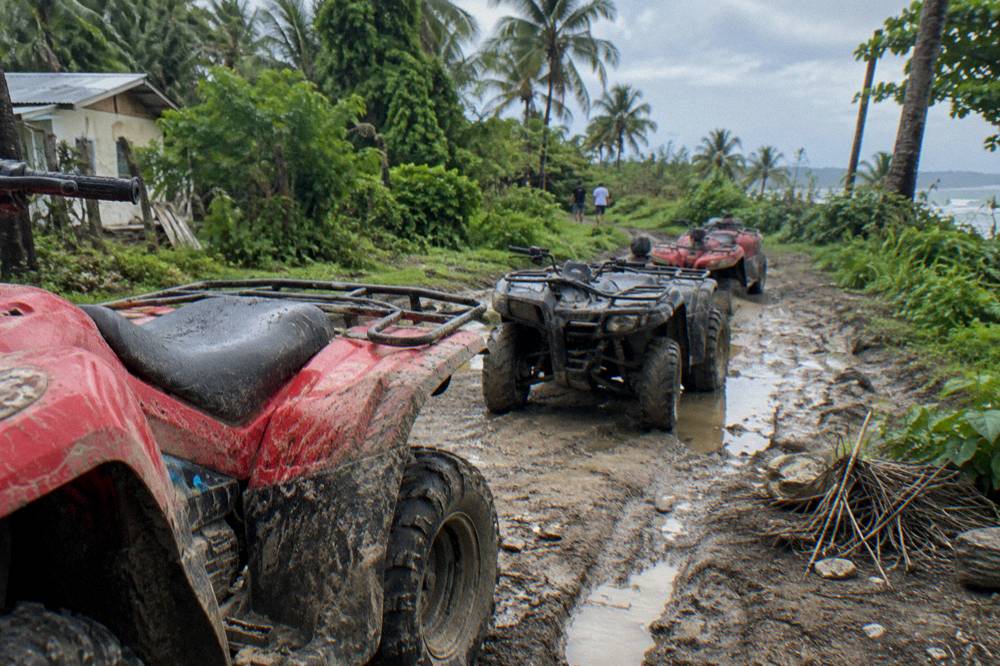 Four wheel ATVs parked on a dirt trail beside tropical vegetation
