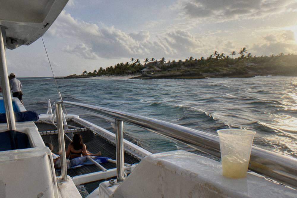 Open double-deck catamaran with passengers sailing along a palm-lined coast