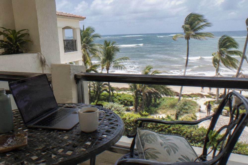 Coffee cup and open laptop on a balcony overlooking a calm Caribbean sea at morning