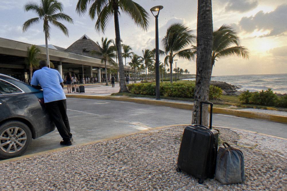 Suitcase and day bag waiting beside a taxi rank under palm trees in evening light