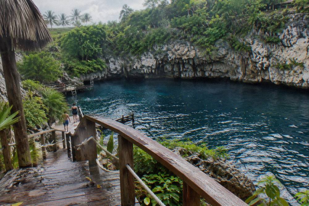 Deep blue freshwater pool at the base of a limestone cliff with wooden walkway along the edge