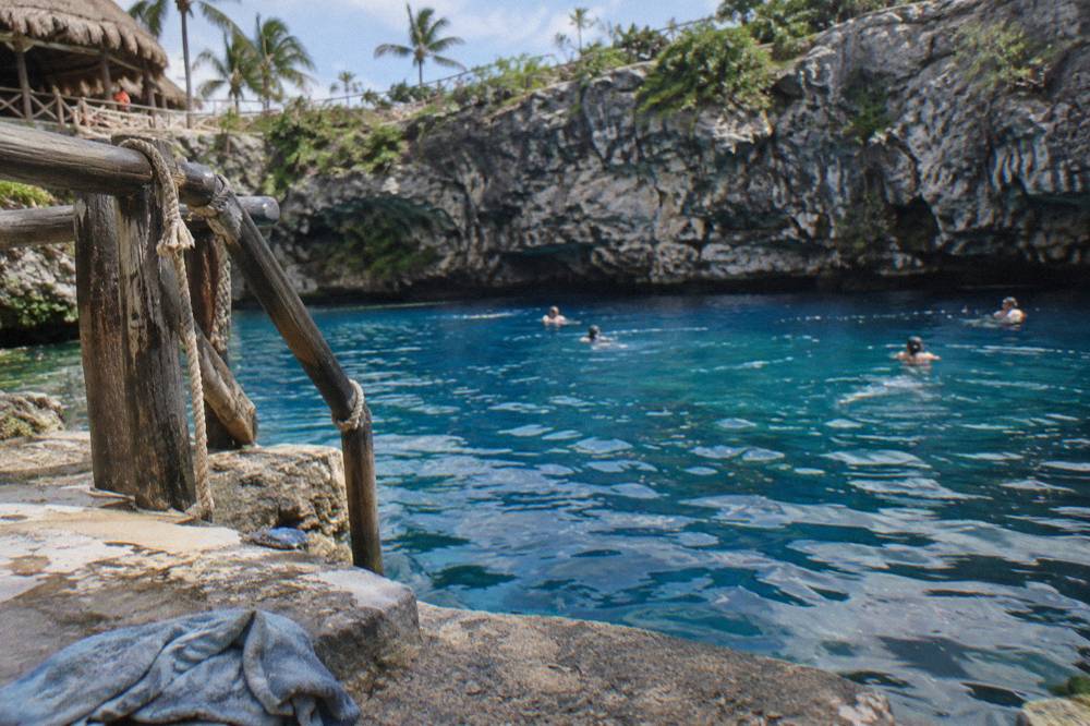 Swimmers floating in bright blue freshwater below a tall limestone cliff wall