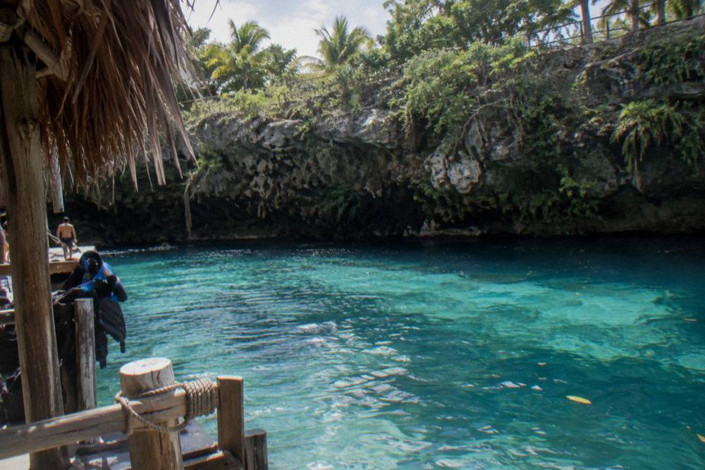 Sunlight striking turquoise water at the base of a shaded limestone cliff
