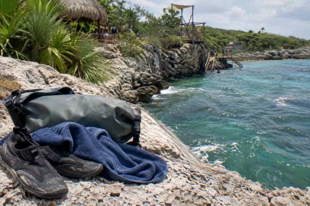 Dry bag, water shoes and towel resting on a bench beside a tropical forest trail