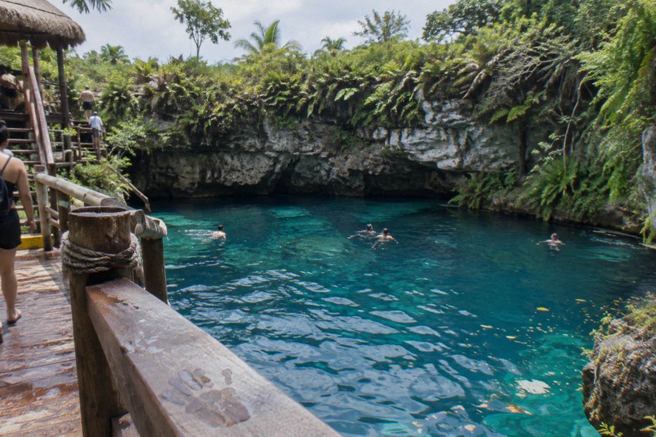 Turquoise water filling a limestone sinkhole surrounded by cliff walls and tropical vegetation