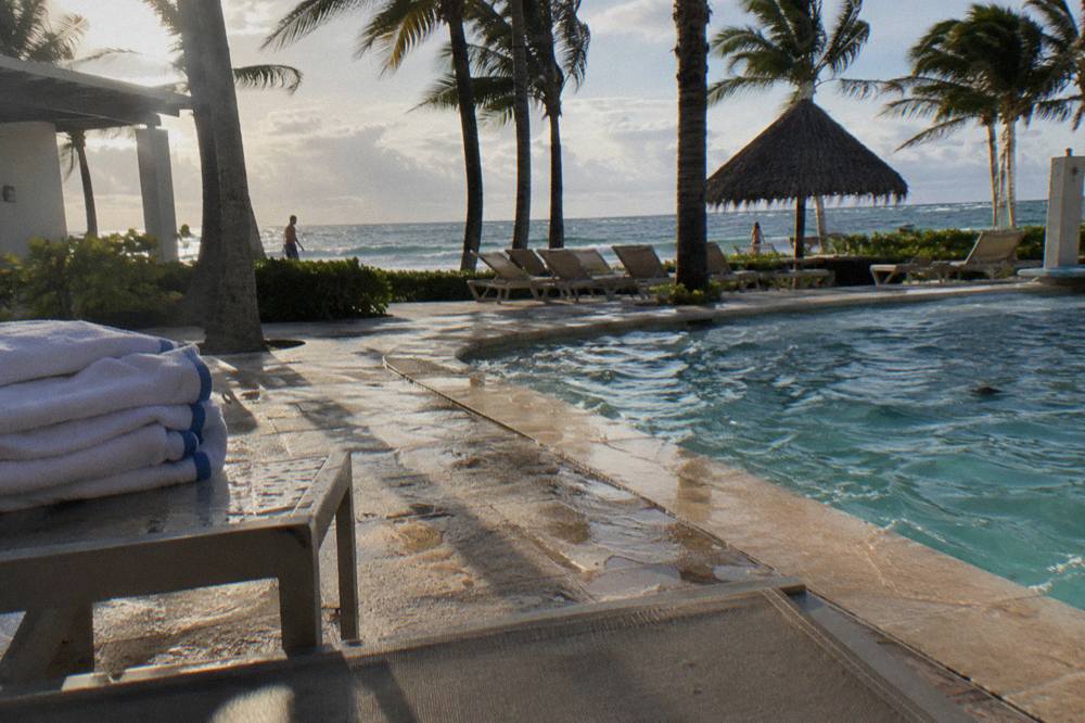 Resort pool deck with palm trees and shaded loungers overlooking the sea