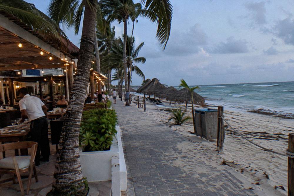Evening beachfront walkway with string lights and restaurant terraces facing the sea