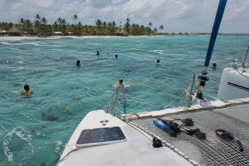 Catamaran anchored in shallow turquoise water with passengers swimming near a sandbar