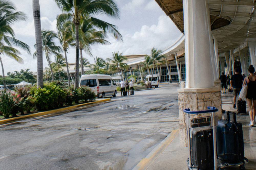 Modern airport terminal exterior with palm trees and shuttle vans waiting at the curb