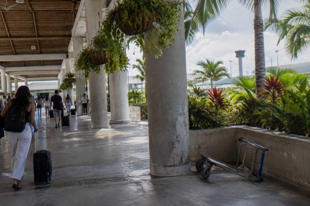 Travelers with luggage walking through a bright open-air airport arrivals corridor