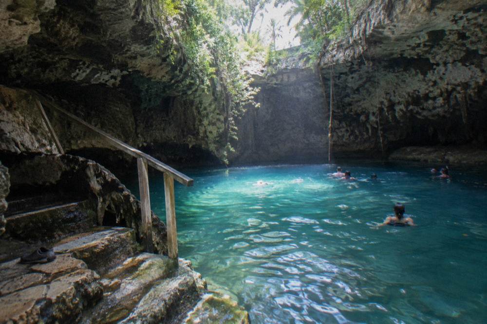 Swimmers in a freshwater cave with turquoise water lit from an opening above
