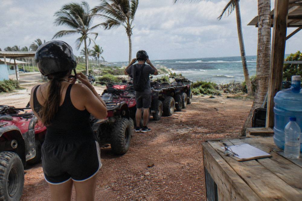Riders fastening helmets beside a row of parked ATVs before departure
