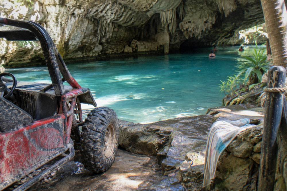 A buggy stopped at the edge of a turquoise freshwater cave surrounded by rock walls