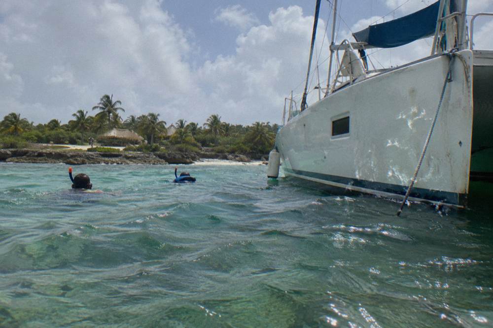 A small group of snorkelers in calm shallow water beside a moored catamaran