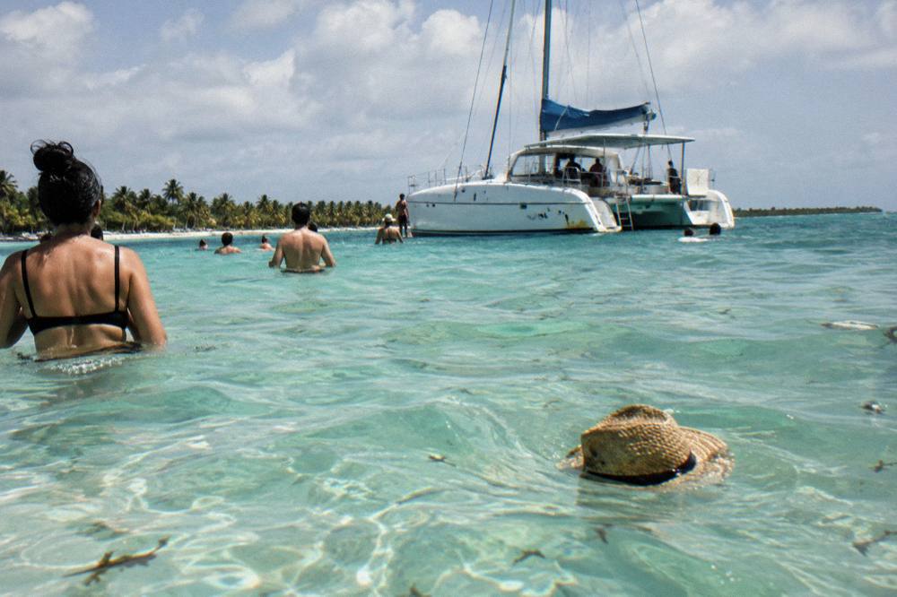 A catamaran moored at a shallow sandbar with guests standing in clear water