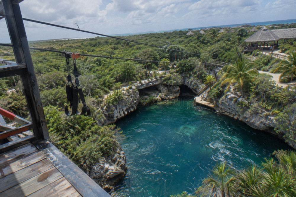 Zipline cables crossing a forested limestone cliff above a turquoise cenote