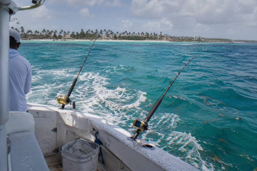 Sportfishing rod in a holder with lines trolling behind a boat on open blue water