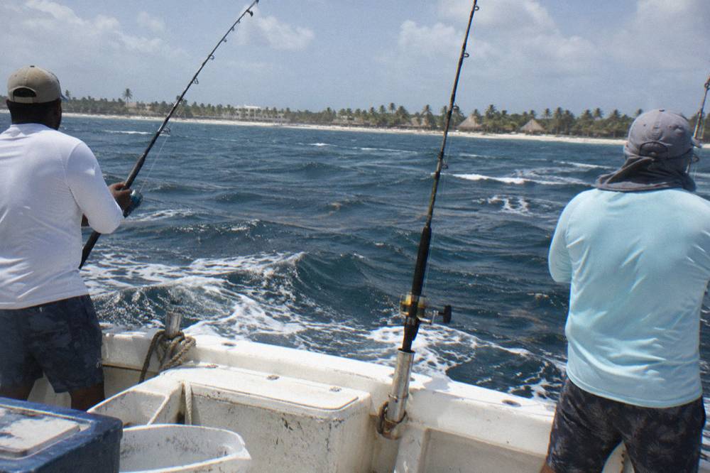 Anglers standing at the stern of a fishing boat holding rods while the coastline sits in the distance