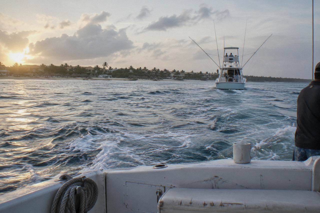 Fishing boat with outriggers heading out over calm blue Caribbean water at sunrise