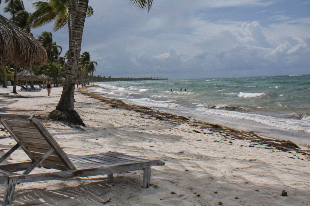 An empty wooden lounge chair on a wide Punta Cana beach under gathering clouds