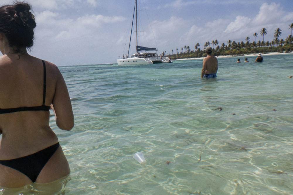 A catamaran anchored near a shallow sandbar with people standing in clear water