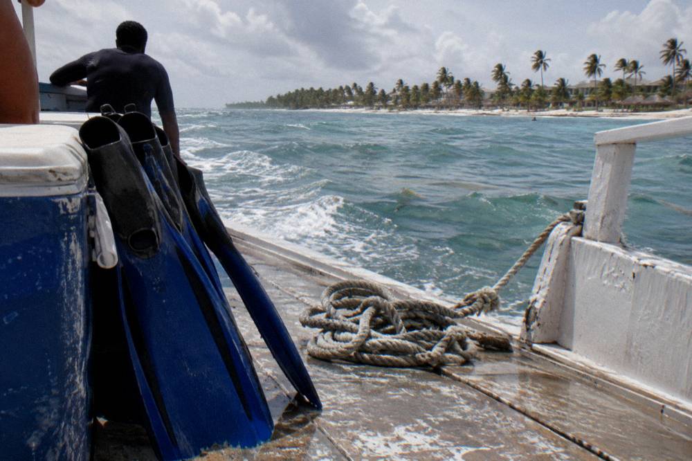 A wooden boat deck with snorkel fins and a cooler against bright sea and sky