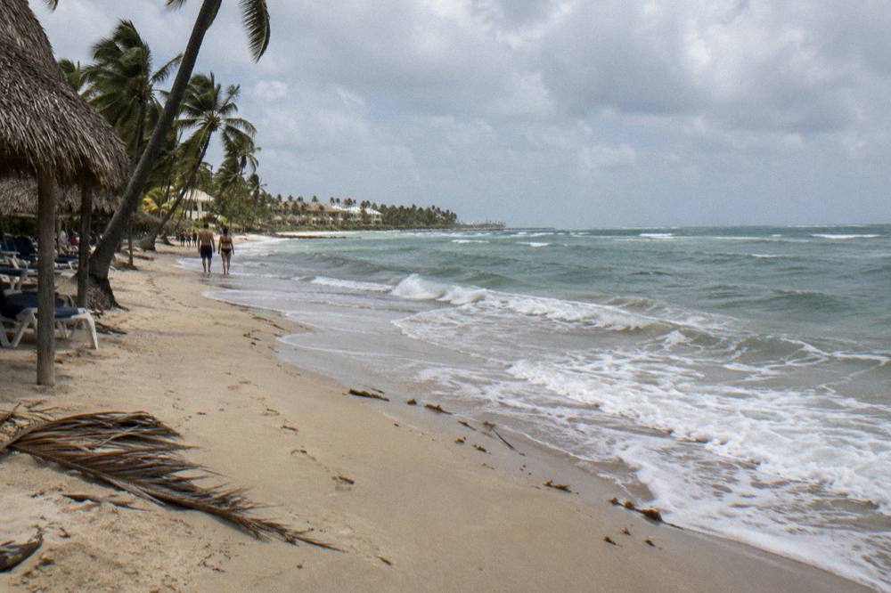 A calm Caribbean beach at midday with pale sand and gentle waves over sand