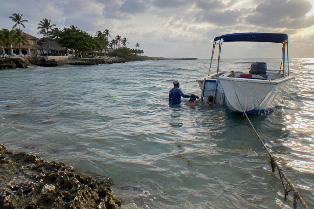 A guide and swimmers together in calm shallow water beside a boat