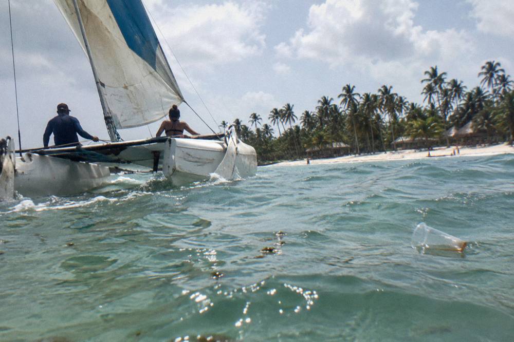 A catamaran sailing on calm turquoise water near a sandbar